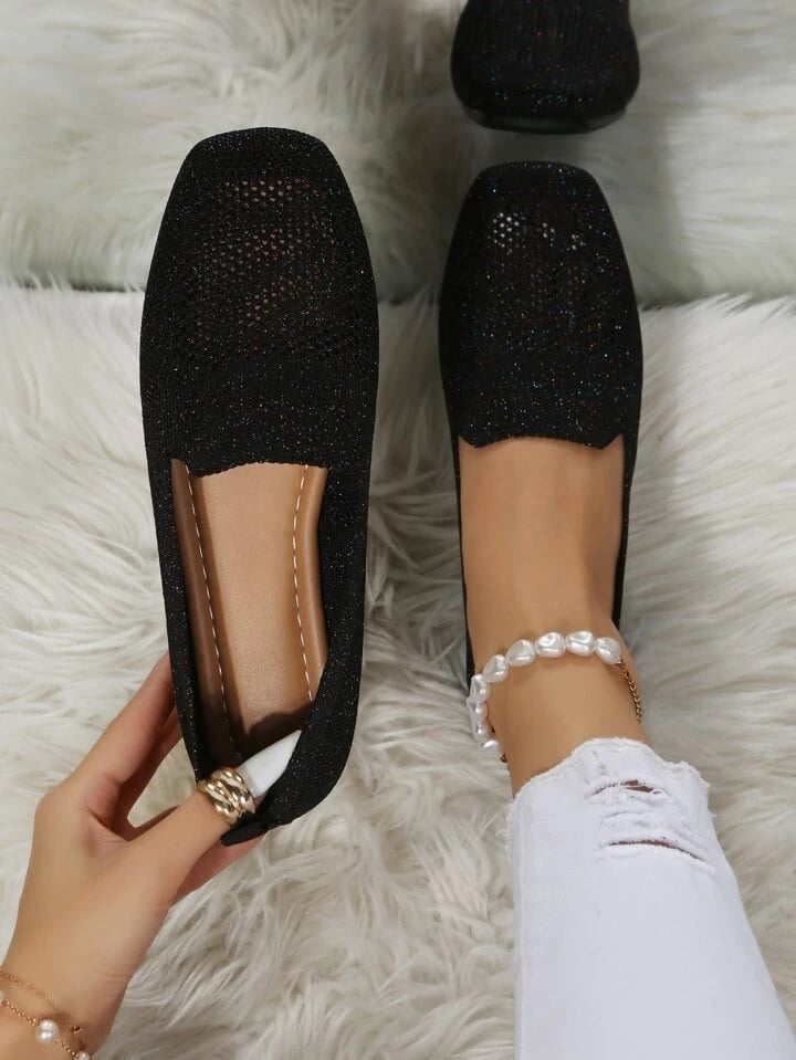 Schwarze Slip-ons aus glitzerndem Mesh von oben, ein Schuh in der Hand mit braunem Fußbett, auf weißem Fell. 1