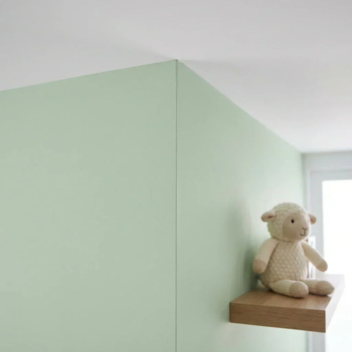 Hellgrün gestrichene Zimmerecke mit sauberer Kante zur weißen Decke, daneben ein Stoffschaf auf einem Holzregal 5