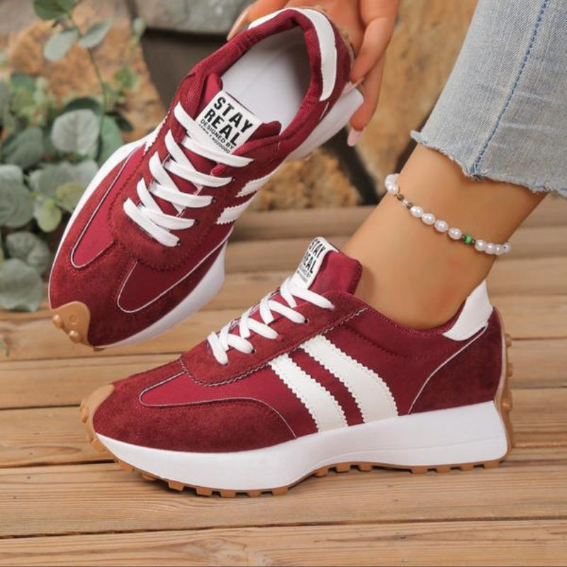 Weinrote Sneaker mit weißen Streifen, getragen zu Jeans und Perlenfußkettchen auf Holzboden 4