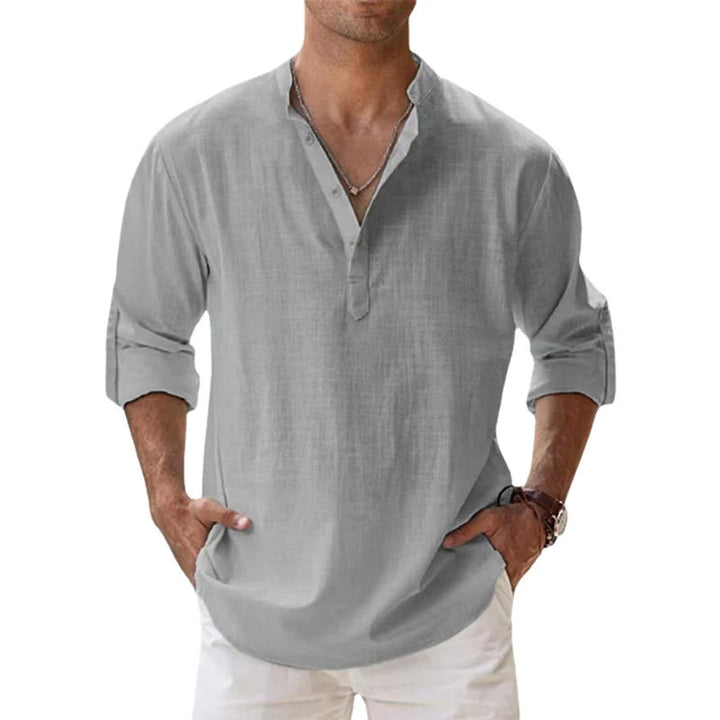 Mann trägt das lockere Henley-Shirt in Hellgrau mit Knopfleiste und aufgerollten Ärmeln, Hände in den Hosentaschen. 6