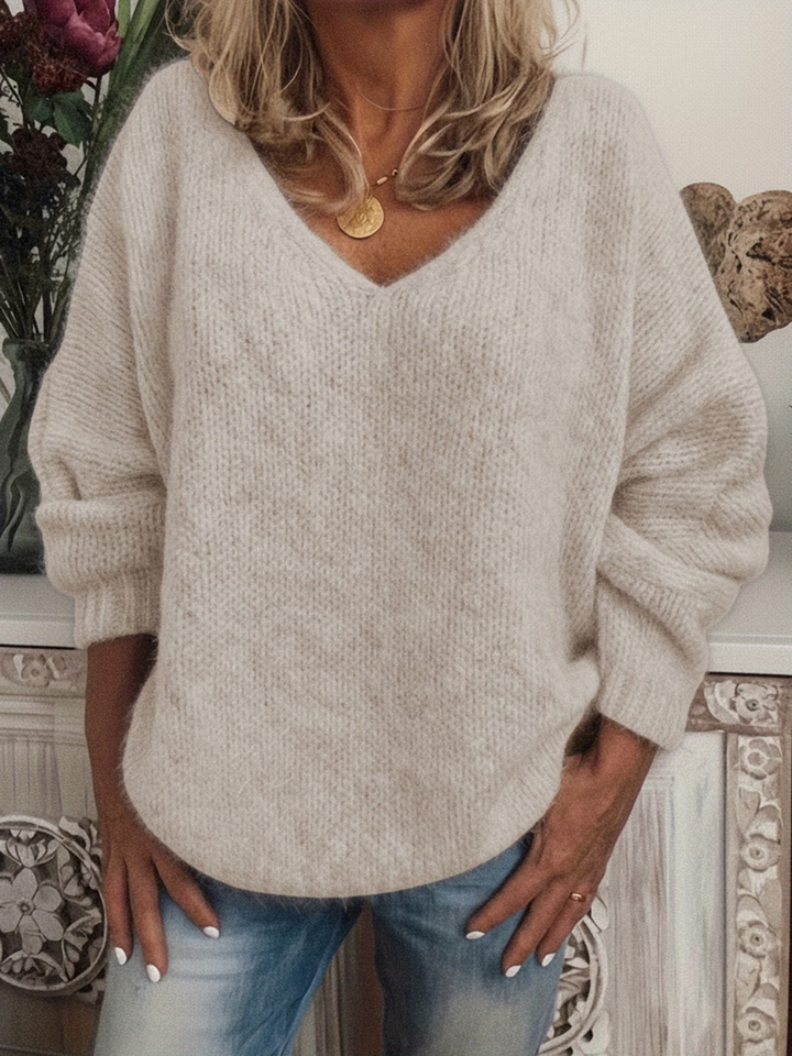 Flauschig wirkender Strickpullover in hellem Beige mit tiefem V-Ausschnitt, lässig getragen zu heller Jeans und goldener Kette. 4