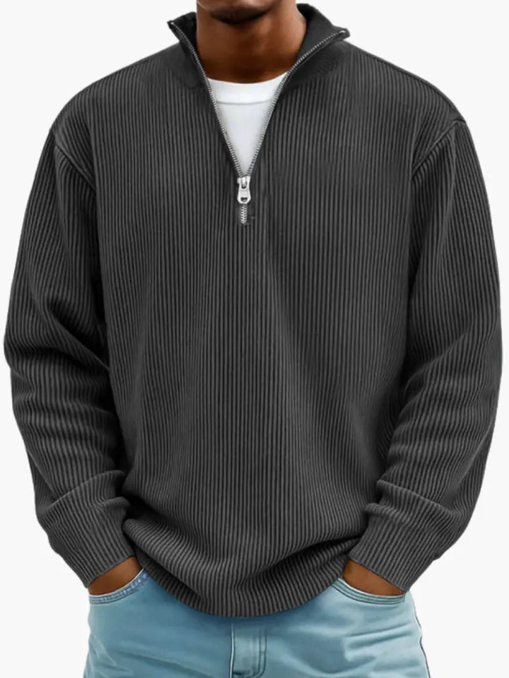 Mann trägt den gerippten Pullover in Anthrazit mit Viertelreißverschluss, Hände in den Taschen einer hellblauen Jeans. 7