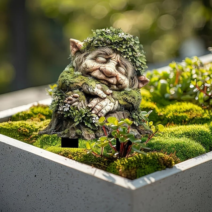 Schlafender Troll mit Blätterkranz und gefalteten Händen auf einem Baumstumpf, in einem Betonkasten mit Moos und Sukkulenten. 4