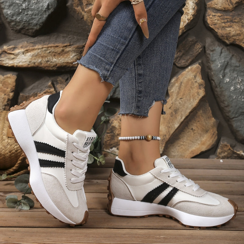 Weiß-beige Sneaker mit schwarzen Streifen, getragen zu Jeans vor einer Steinwand 5