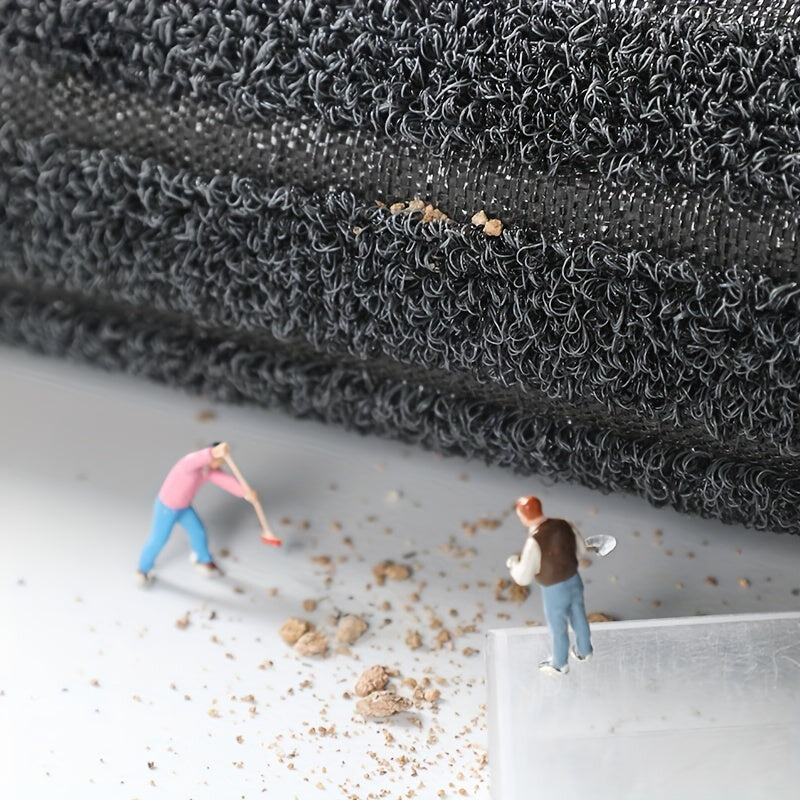 Aufgerollte Mattenkante mit Blick auf Faserschlingen und Gewebeträger, davor Miniaturfiguren, die herabgefallenen Schmutz wegkehren. 6