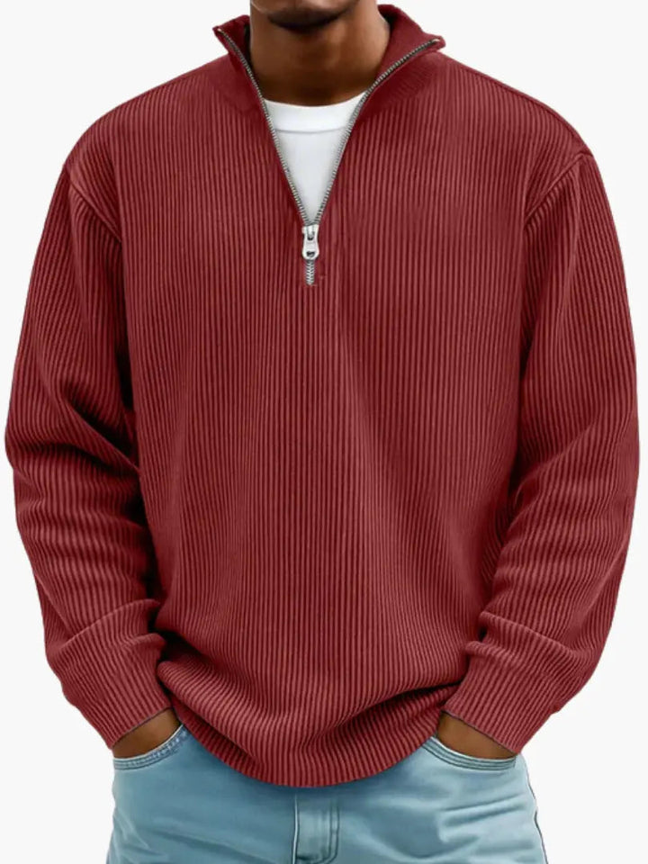 Mann trägt den gerippten Pullover in Weinrot mit Reißverschlusskragen über einem weißen Shirt, Frontansicht mit Händen in den Taschen. 10