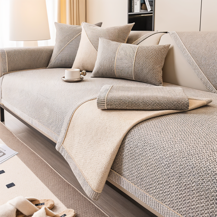 Sofaschutz in Beige-Grau, mit umgeschlagener Ecke und aufgelegtem gefaltetem Stück, das die glatte helle Unterseite zeigt. 3
