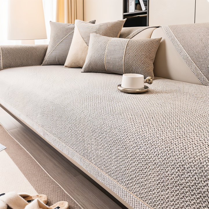 Nahaufnahme des beige-grau gewebten Sofabezugs auf der Sitzfläche mit Zierkante, Kissen und weißer Tasse im Hintergrund. 5
