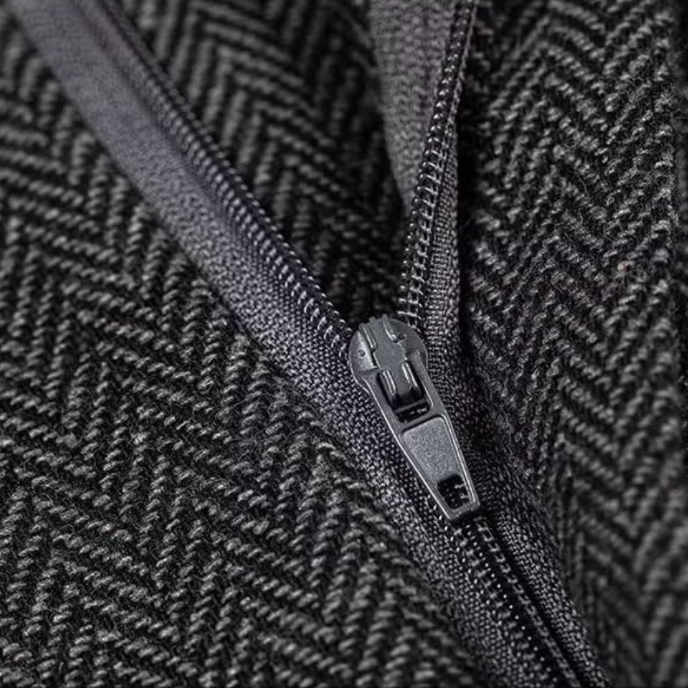 Schwarzer Reißverschluss auf grauem Fischgrätstoff, Nahaufnahme, Textil, Modeaccessoire.