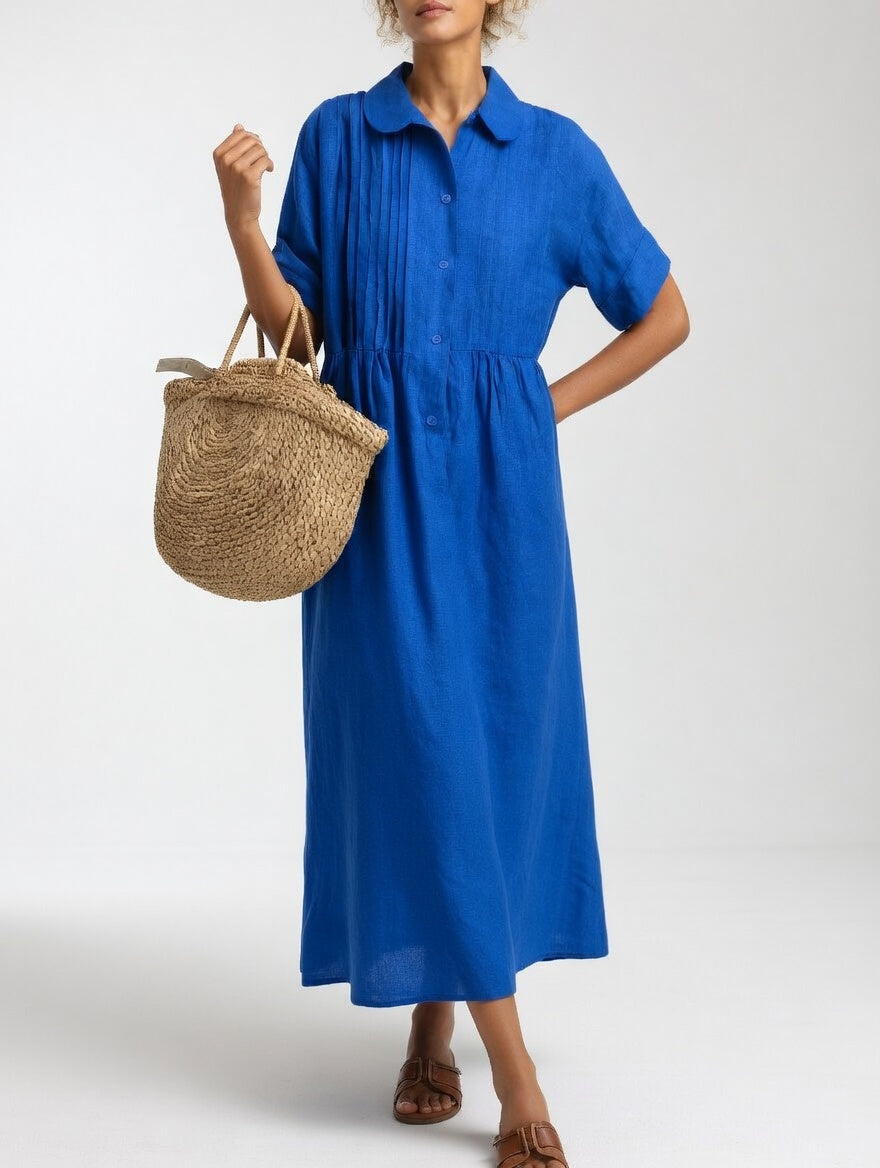 Das Hemdkleid in kräftigem Königsblau von vorn, mit Strohtasche am Arm und einer Hand an der Hüfte. 3
