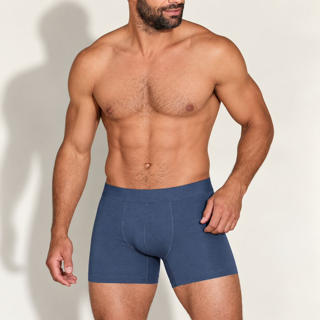 Muskulöser bärtiger Mann trägt die blaugraue Boxershorts mit breitem Bund, frontal vor hellem Hintergrund, Hand an der Hüfte. 1