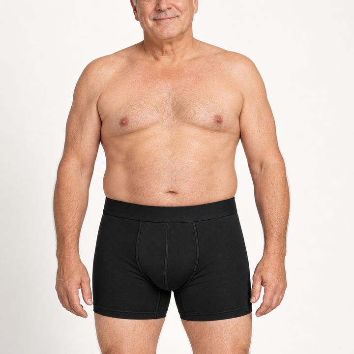 Älterer, lächelnder Mann trägt die schwarze Boxershorts mit Eingriff-Naht frontal vor weißem Hintergrund. 2