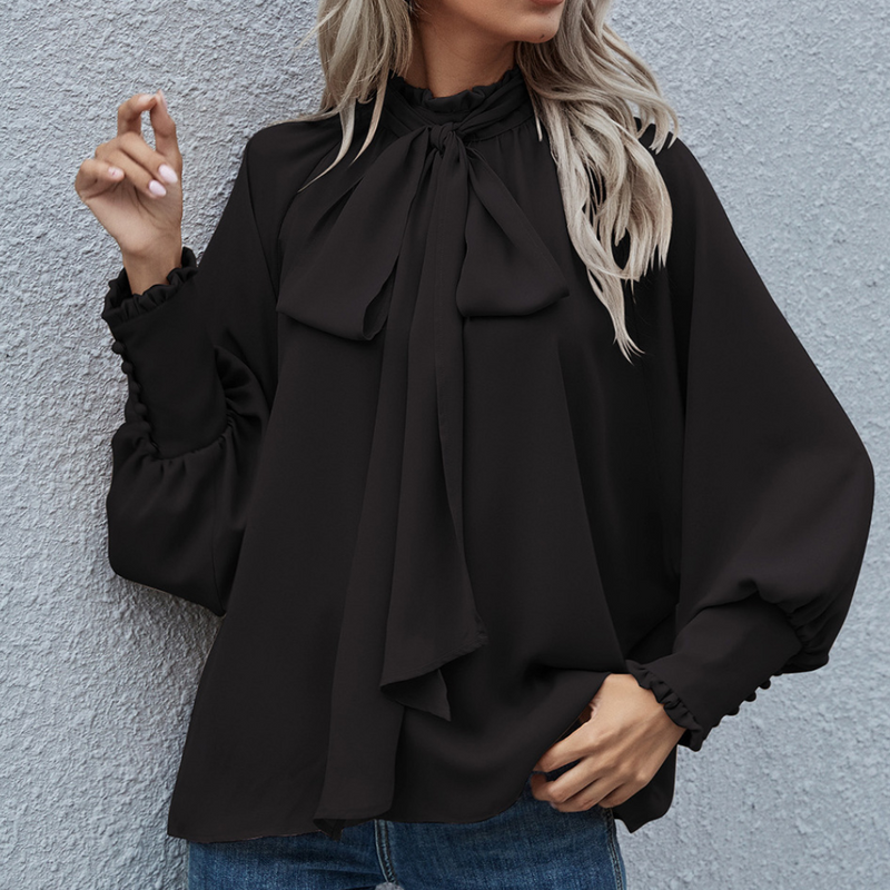 Frau in schwarzer Bluse mit Schleife, lange Ärmel, elegante Damenmode, vor grauer Wand.