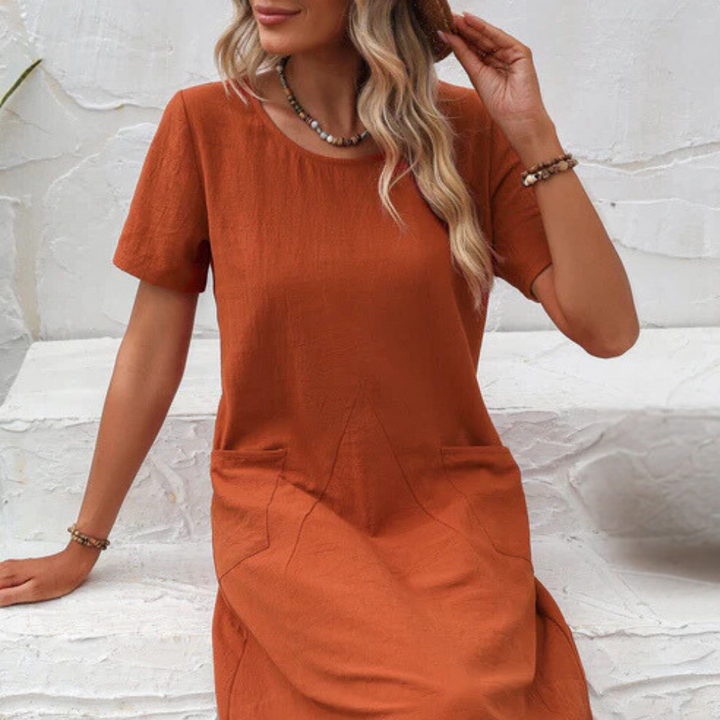 Frau in orangefarbenem Leinenkleid, Sommermode, lässiger Stil, Accessoires, weiße Wand.