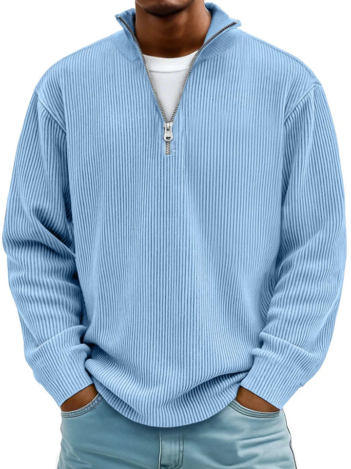 Mann trägt den Rippstrickpullover in Hellblau mit Reißverschlusskragen, Hände in den Hosentaschen, weißes Shirt darunter 1