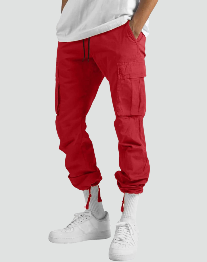 Model trägt die rote Cargohose frontal mit am Saum zusammengezogenen Beinabschlüssen und sichtbaren Kordeln, dazu weiße Socken und Sneaker. 11
