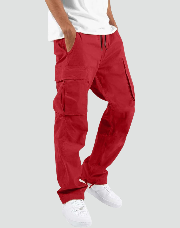 Model trägt die rote Cargohose mit Seitentaschen und Kordelzug zu weißem T-Shirt und weißen Sneakern, Seitenansicht vor grauem Hintergrund. 10