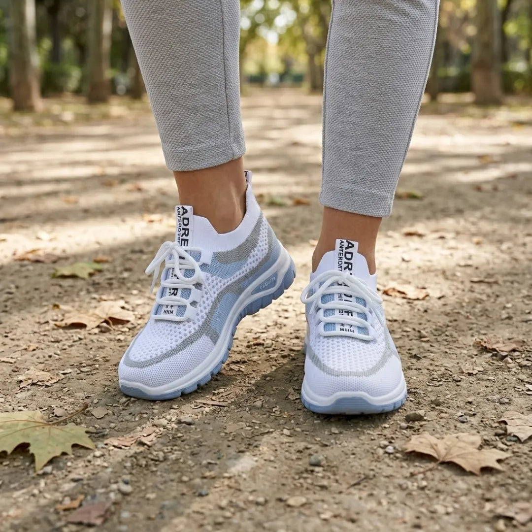 Weiß-hellblaue Mesh-Sneaker an den Füßen einer Trägerin im Park, kombiniert mit grauer Hose, auf Waldboden mit Herbstlaub. 2