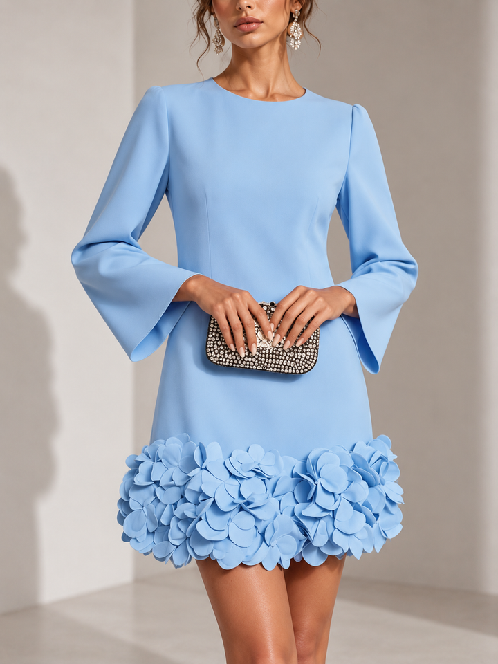 Hellblaues Kleid in Frontansicht mit ausgestellten Ärmeln und plastischen Blüten am Saum, dazu eine Strass-Clutch. 5