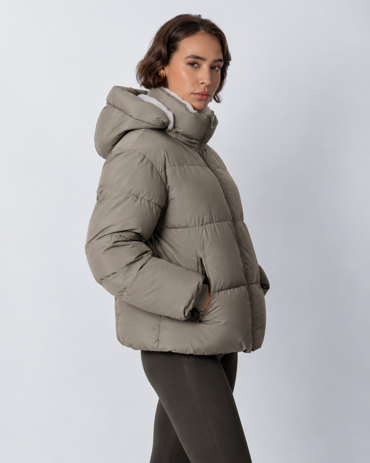 Seitenansicht der graubraunen Steppjacke mit Kapuze und Reiverschlusstasche, getragen mit dunklen Leggings 19