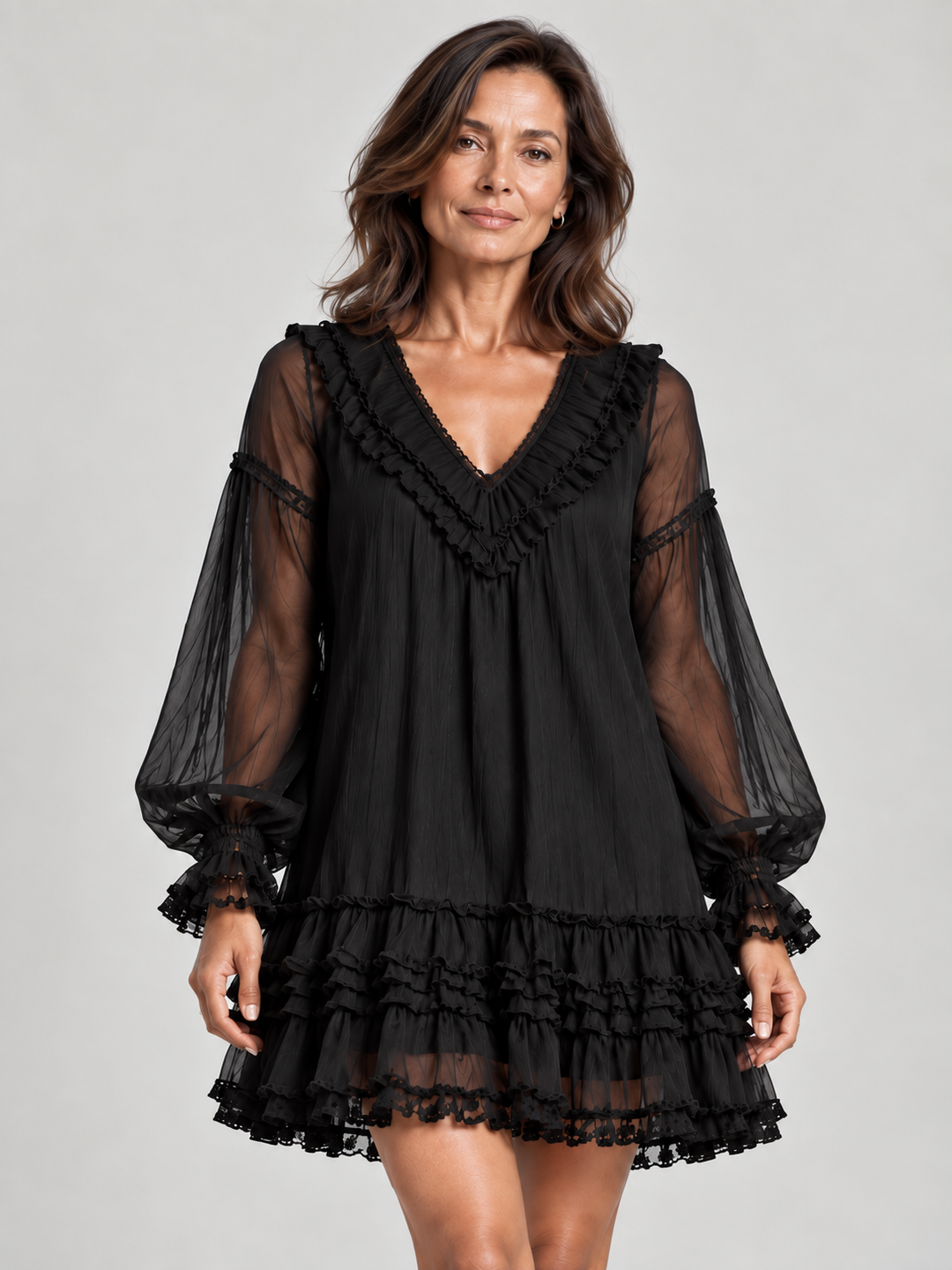 Frau in schwarzem Minikleid mit gerüschtem V-Ausschnitt, transparenten Ballonärmeln und gestuftem Rüschensaum, Halbfigur von vorn. 1