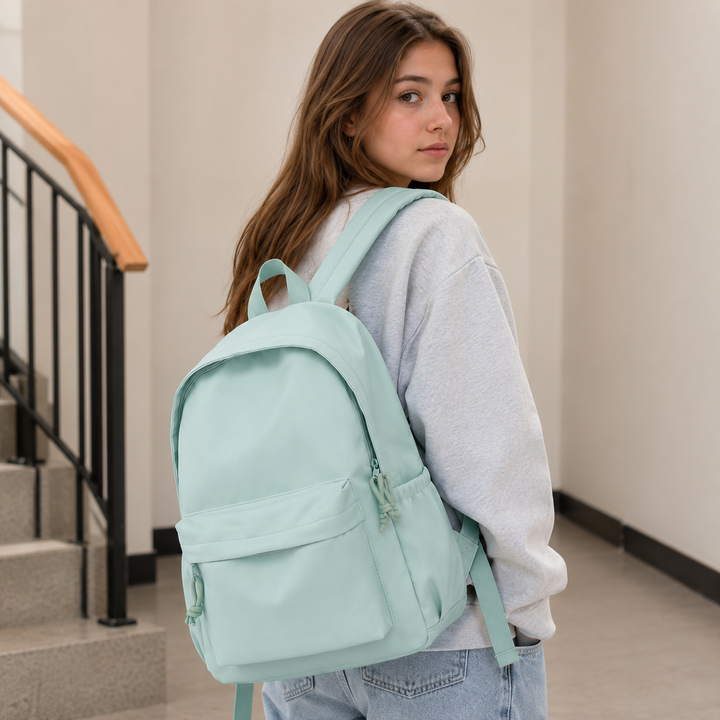 Junge Frau trägt den mintgrünen Rucksack über einer Schulter, hellgraues Sweatshirt und Jeans, im Treppenhaus mit Blick zurück zur Kamera. 3
