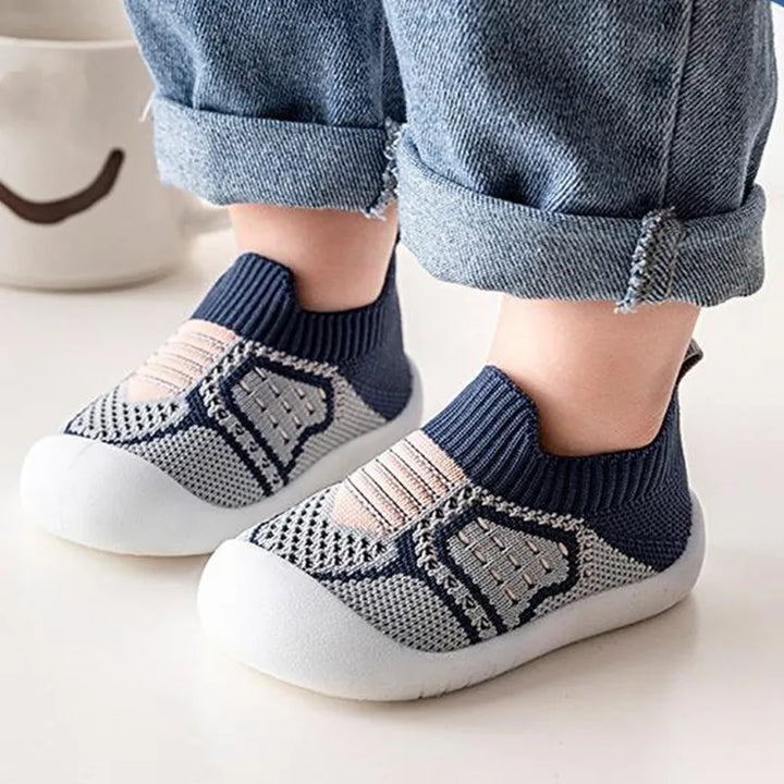 Kinderfüße in marineblau-grauen Strick-Slippern mit weißer Gummisohle, getragen mit umgekrempelter Jeans. 14