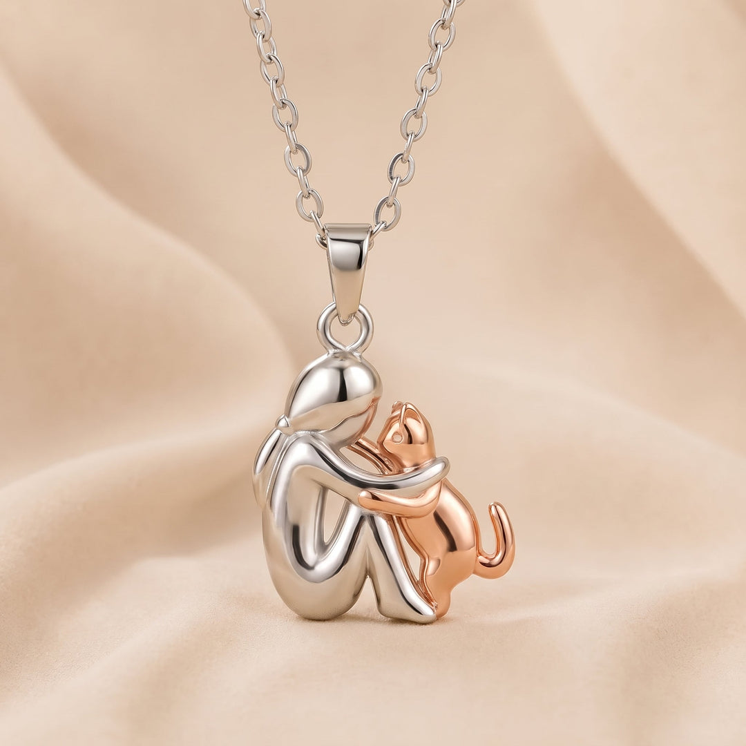 Silberfarbene Figur mit roségoldfarbener Katze, die die Pfoten an sie legt, Anhänger an Kette auf Stoff. 4