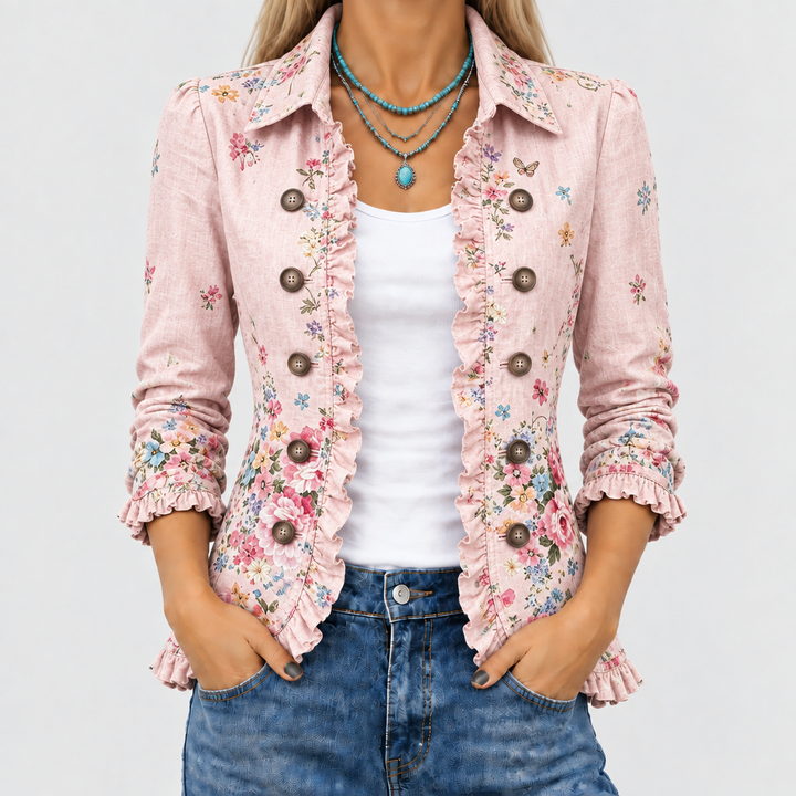 Nahaufnahme des Oberkörpers: rosa Blumenjacke mit Rüschenkante, Knopfreihen und Kragen, offen getragen über weißem Top und Jeans. 1