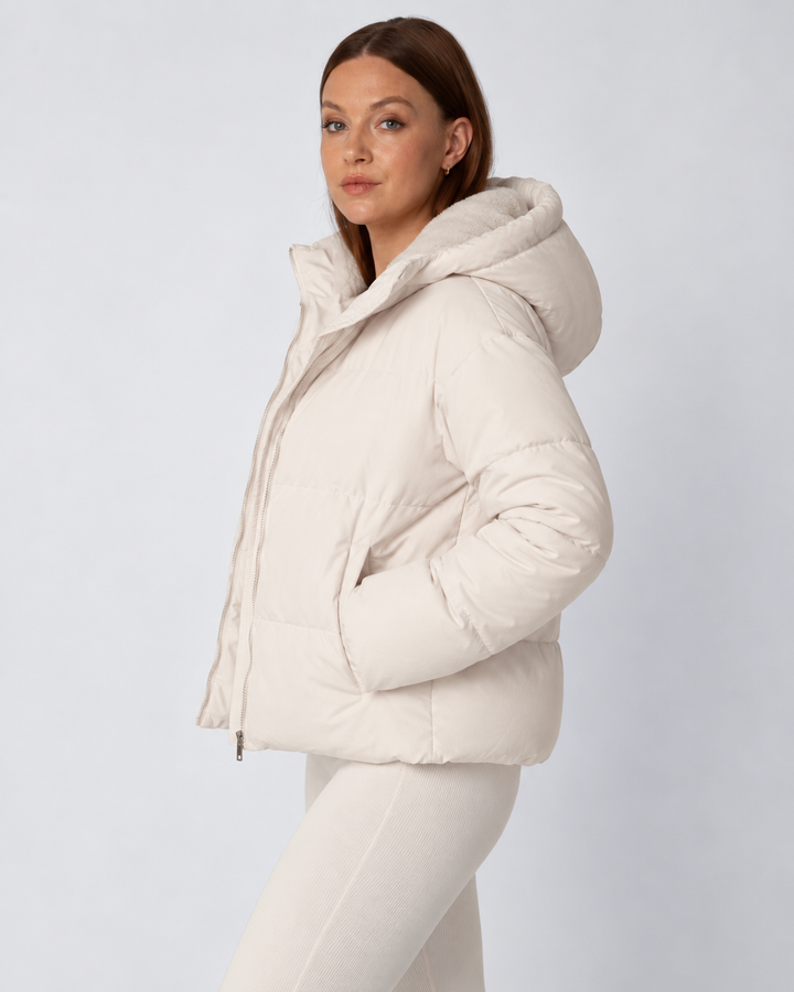 Seitenansicht der cremefarbenen Steppjacke mit aufgesetzter Kapuze, Reiverschluss und Hand in der Seitentasche 3