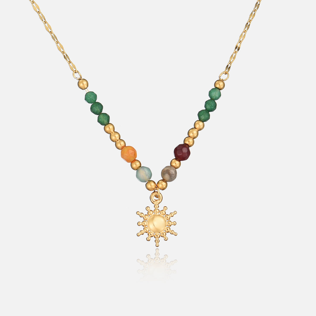 Goldene Kette mit grünen, orangen und roten Perlen und kleinem Sonnenanhänger, frontal vor hellem Hintergrund 1