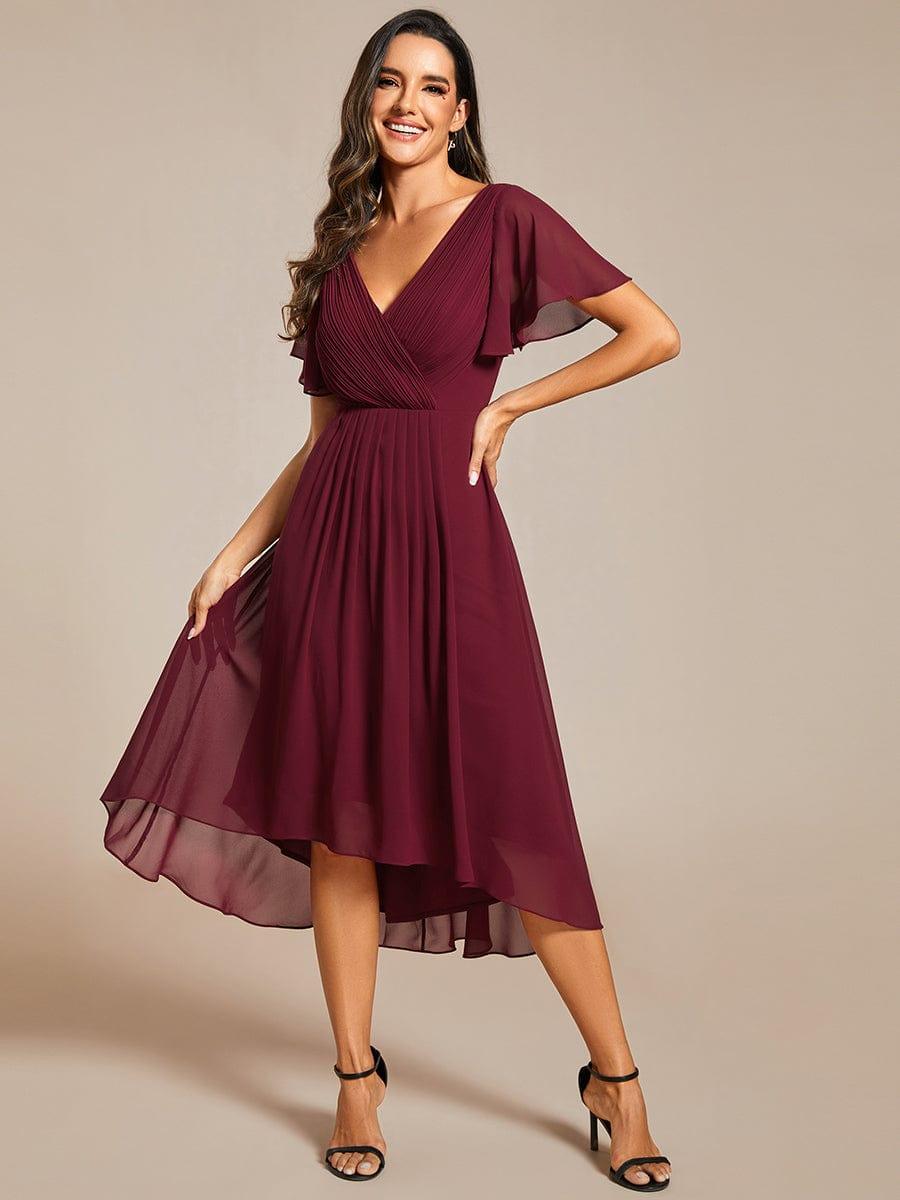 Model im weinroten Chiffonkleid hebt mit einer Hand den Rock an, andere Hand an der Hüfte, schwarze Sandalen. 48