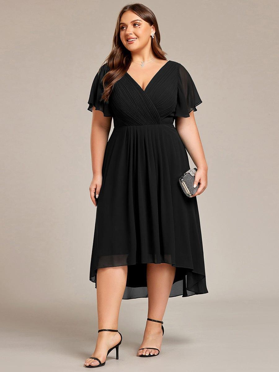 Curvy Model im schwarzen Kleid frontal mit kleiner Glitzerclutch in der Hand, gerafftes Oberteil und knielanger Hoch-Tief-Saum. 30