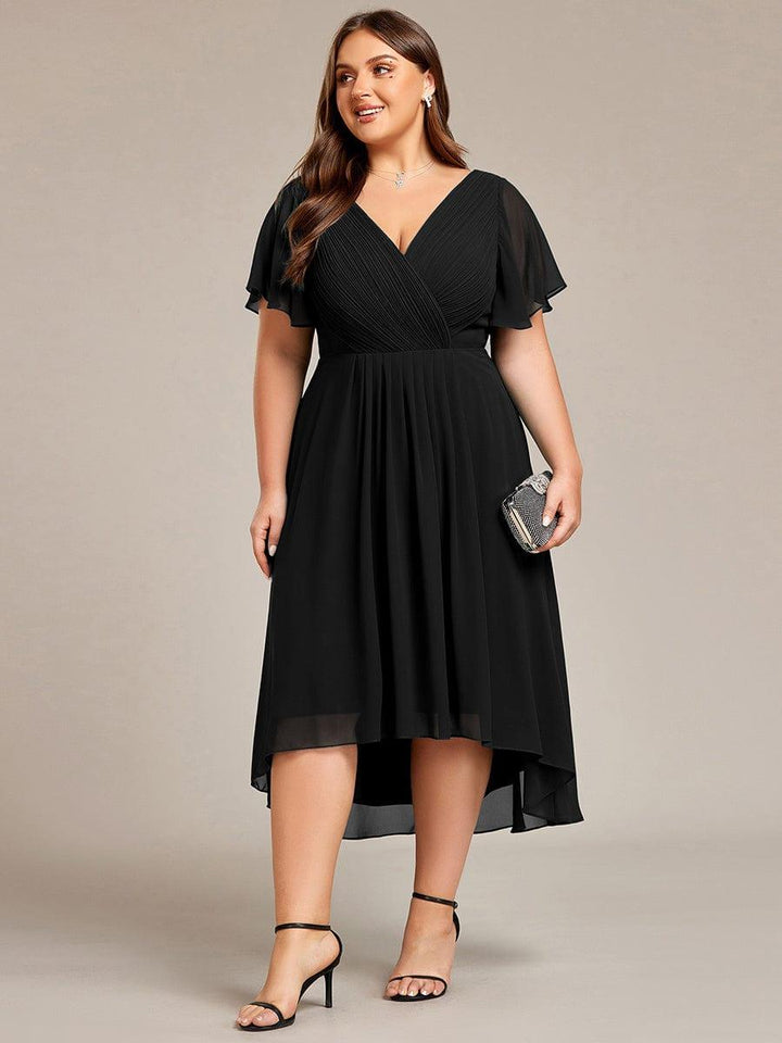 Curvy Model im schwarzen Kleid frontal mit kleiner Glitzerclutch in der Hand, gerafftes Oberteil und knielanger Hoch-Tief-Saum. 30
