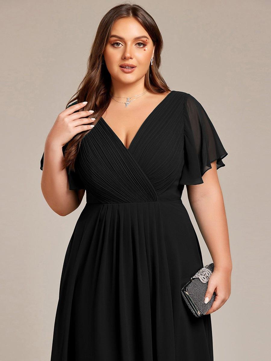 Nahaufnahme des schwarzen Oberteils an einem Curvy Model, gerafftes V-Dekolleté und Flatterärmel, dazu eine schwarze Glitzerclutch in der Hand. 28