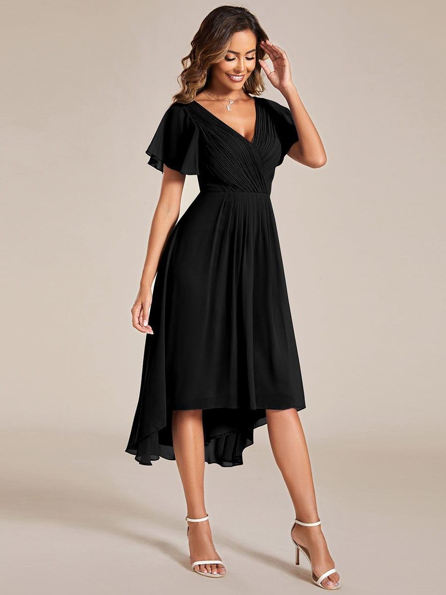 Lächelndes Model im schwarzen Kleid in leichter Drehung, eine Hand am Kopf, der fließende Chiffonrock mit Hoch-Tief-Saum ist gut zu sehen. 25