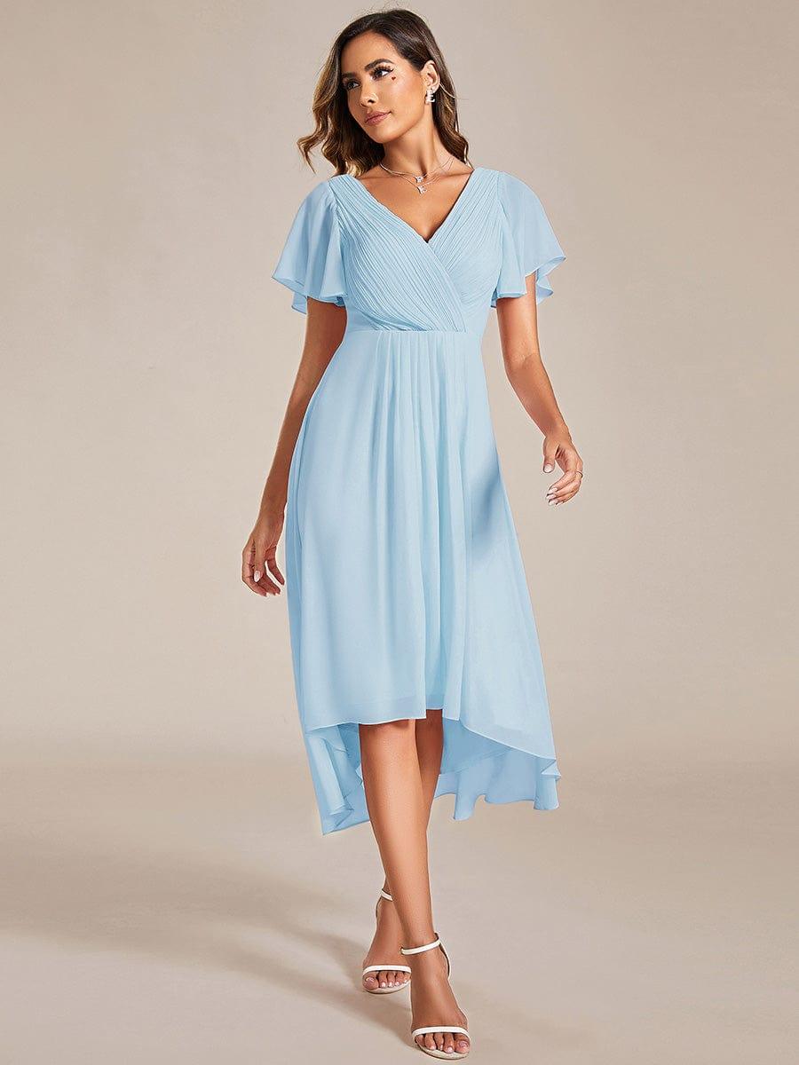 Model in hellblauem Chiffonkleid mit V-Ausschnitt, Flatterärmeln und asymmetrischem Saum, kombiniert mit weißen Riemchensandaletten, frontal fotografiert. 84