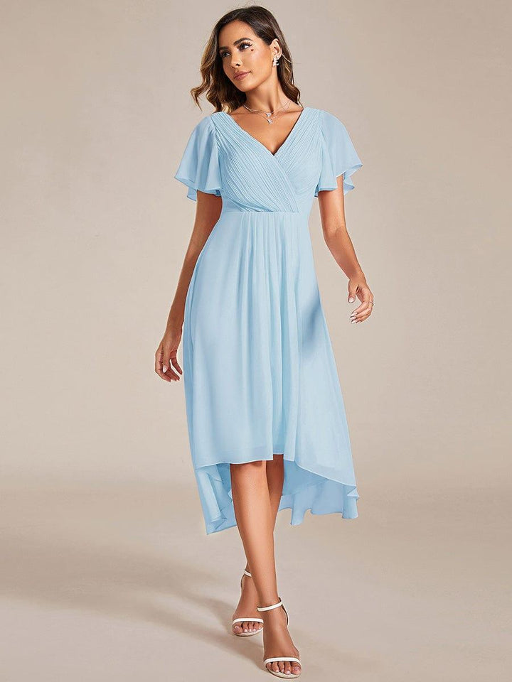 Model in hellblauem Chiffonkleid mit V-Ausschnitt, Flatterärmeln und asymmetrischem Saum, kombiniert mit weißen Riemchensandaletten, frontal fotografiert. 84