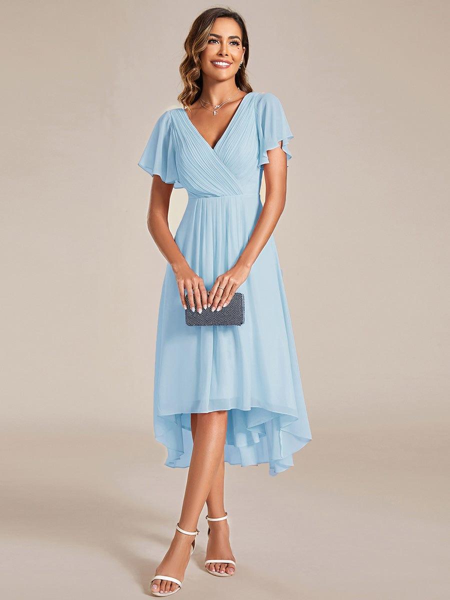 Model in hellblauem Kleid hält eine dunkle Glitzer-Clutch mit beiden Händen und trägt weiße Sandaletten. 87