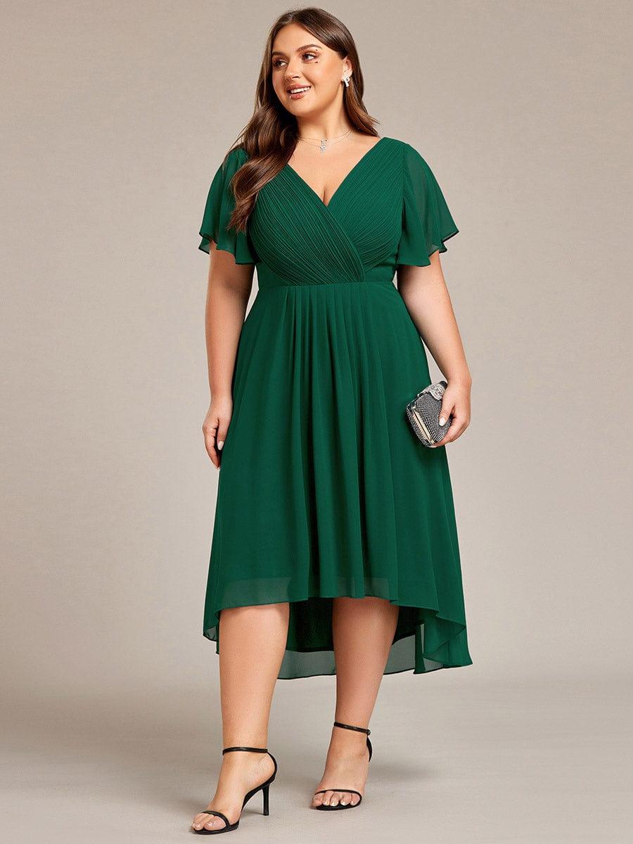 Curvy Model im dunkelgrünen Chiffonkleid frontal mit kleiner Glitzerclutch, gerafftes Oberteil, Flatterärmel und knielanger Hoch-Tief-Saum. 40