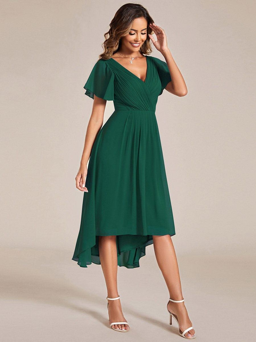 Dunkelgrünes Kleid in schräger Seitenansicht, Model lächelt und fasst sich ans Haar, der Chiffonrock fällt weich. 14