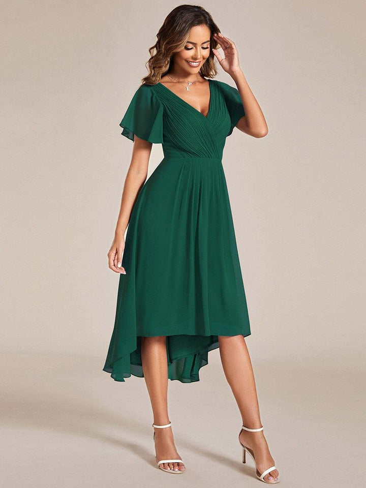 Dunkelgrünes Kleid in schräger Seitenansicht, Model lächelt und fasst sich ans Haar, der Chiffonrock fällt weich. 14