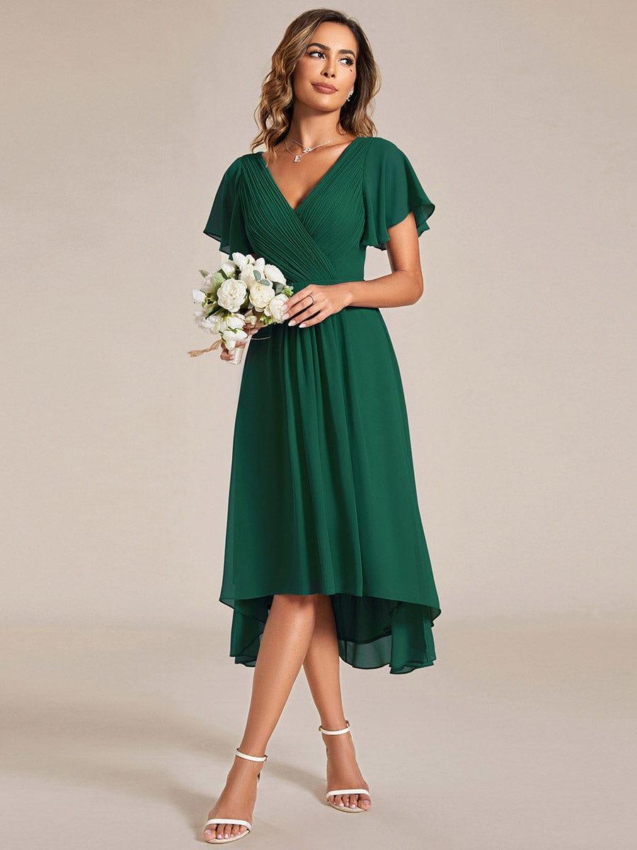 Dunkelgrünes Kleid mit weißem Blumenstrauß in der Hand, Model blickt zur Seite, der asymmetrische Saum ist sichtbar. 13