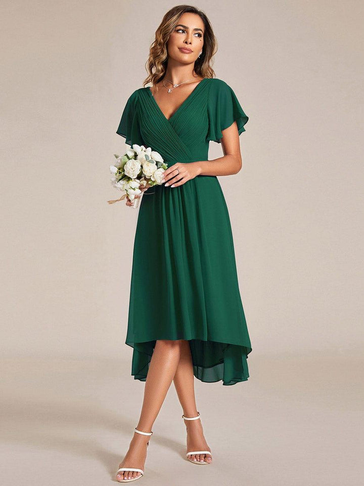 Dunkelgrünes Kleid mit weißem Blumenstrauß in der Hand, Model blickt zur Seite, der asymmetrische Saum ist sichtbar. 13