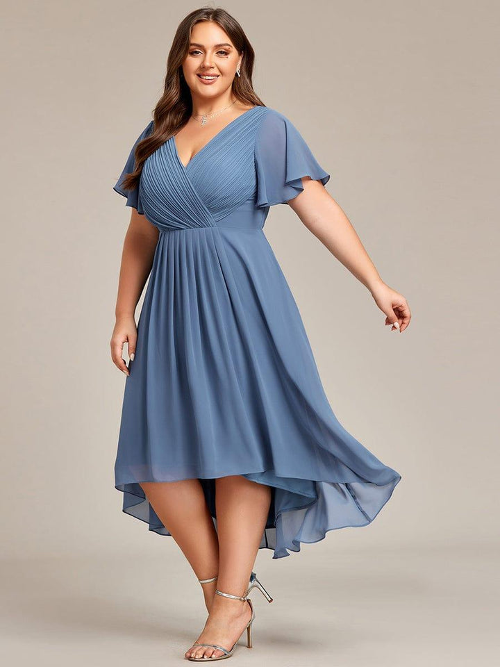 Staubblaues Chiffonkleid am Plus-Size-Model in Schrittbewegung, der asymmetrische Saum schwingt, dazu silberne Riemchensandalen. 45