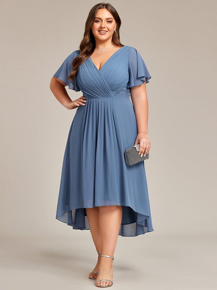 Plus-Size-Model in staubblauem Chiffonkleid, Hand in der Hüfte, mit schwarzer Strass-Clutch und silbernen Sandalen, Vorderansicht. 44