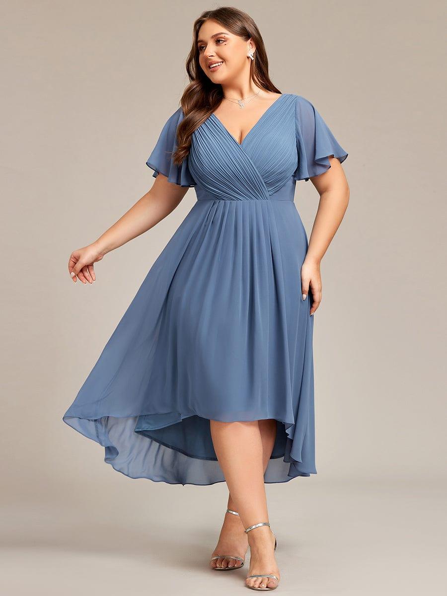 Plus-Size-Model im staubblauen Chiffonkleid mit Wickeloptik, Flatterärmeln und Vorne-kurz-hinten-lang-Saum, in Bewegung fotografiert, silberne Sandalen. 41