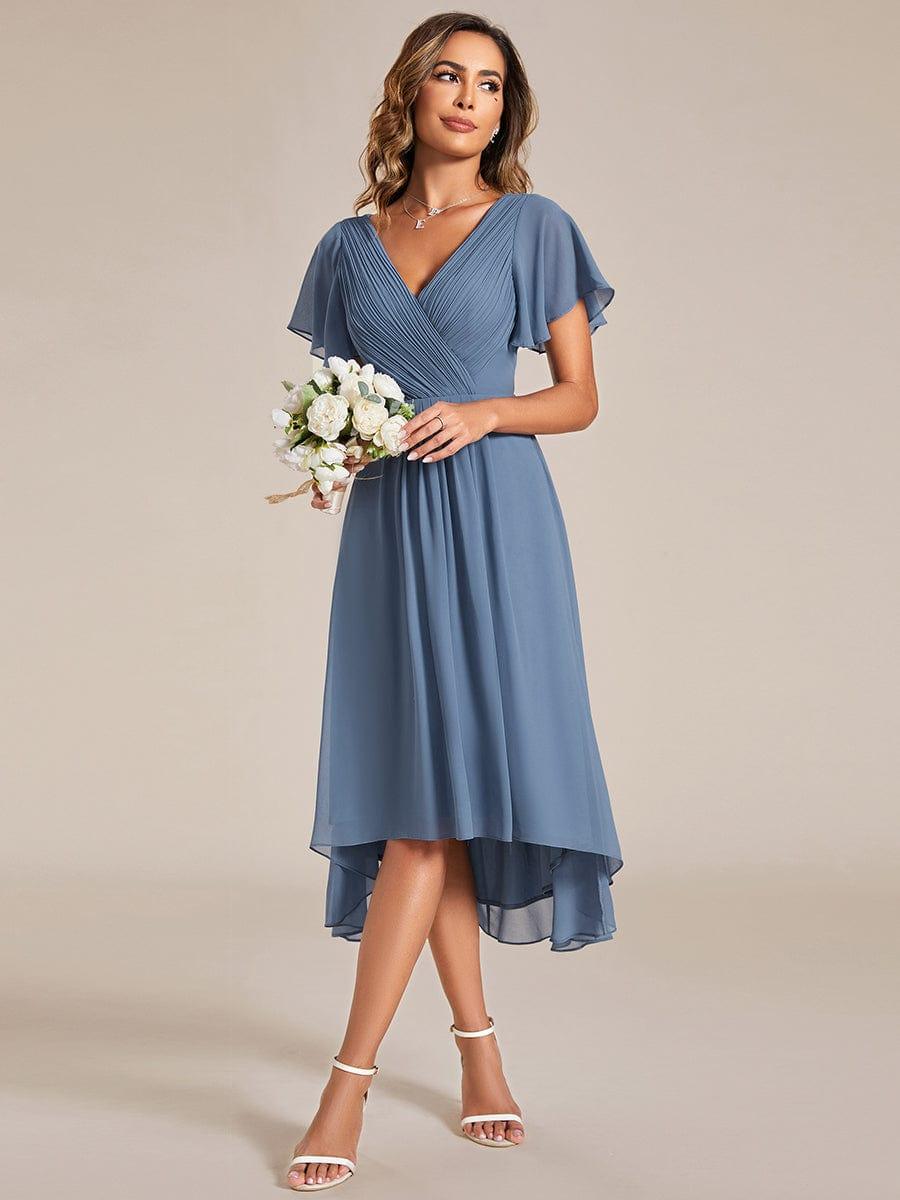Staubblaues Kleid getragen von einem Model mit weißem Blumenstrauß, seitlich fotografiert, der Hoch-Tief-Saum ist gut zu erkennen. 8