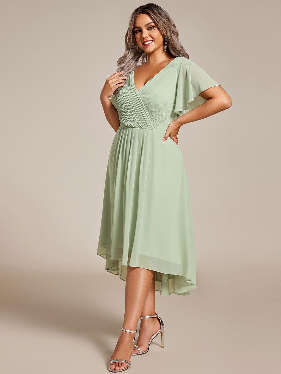 Curvy Model in mintgrünem Chiffonkleid mit plissiertem V-Ausschnitt, Flatterärmeln und Vokuhila-Saum, Hand an der Hüfte, silberne Sandaletten. 81