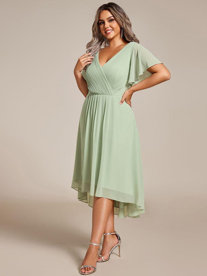 Curvy Model in mintgrünem Chiffonkleid mit plissiertem V-Ausschnitt, Flatterärmeln und Vokuhila-Saum, Hand an der Hüfte, silberne Sandaletten. 81